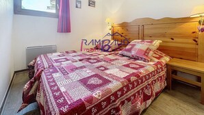 Ein Schlafzimmer mit einem Holzkopfteil, einer gemusterten Bettdecke, einem Nachttisch mit Lampe und einem Fenster mit Vorhängen.