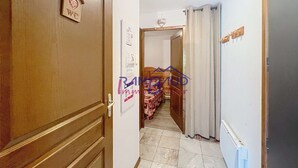 Ein schmaler Korridor mit einer Holztür links, einer weißen Wand mit einem gerahmten Bild und einem Bett, das in der Ferne sichtbar ist.