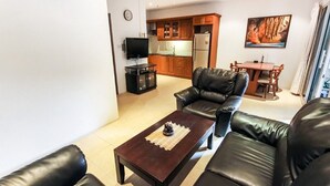 Un salon avec une table basse marron foncé, un canapé en cuir noir et un téléviseur posé sur un meuble.