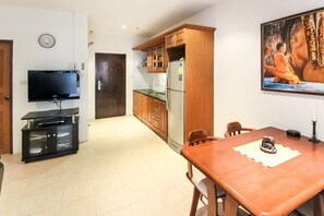 Une cuisine compacte avec des meubles en bois, un réfrigérateur et un téléviseur à écran plat fixé au mur.