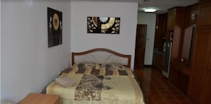 A bedroom with a bed, a wooden headboard, a nightstand, and a wall-mounted artwork. - Thep Thip Mansion F5 R5003 (Pattaya)