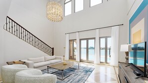 A spacious living room with a staircase, a large window with a view, a flat-screen TV, and a coffee table. - Maison Privee - Palm Jumeirah Beach Front XL Villa w/Prvt Pool (Dubai)