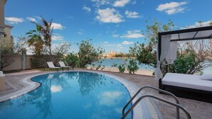 A swimming pool with lounge chairs and a view of a building across the water. - Maison Privee - Palm Jumeirah Beach Front XL Villa w/Prvt Pool (Dubai)