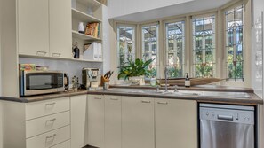 Une cuisine moderne équipée d’un lave-vaisselle, d’un four à micro-ondes et d’une machine à café. Une fenêtre aux vitraux offre une vue sur la verdure environnante.