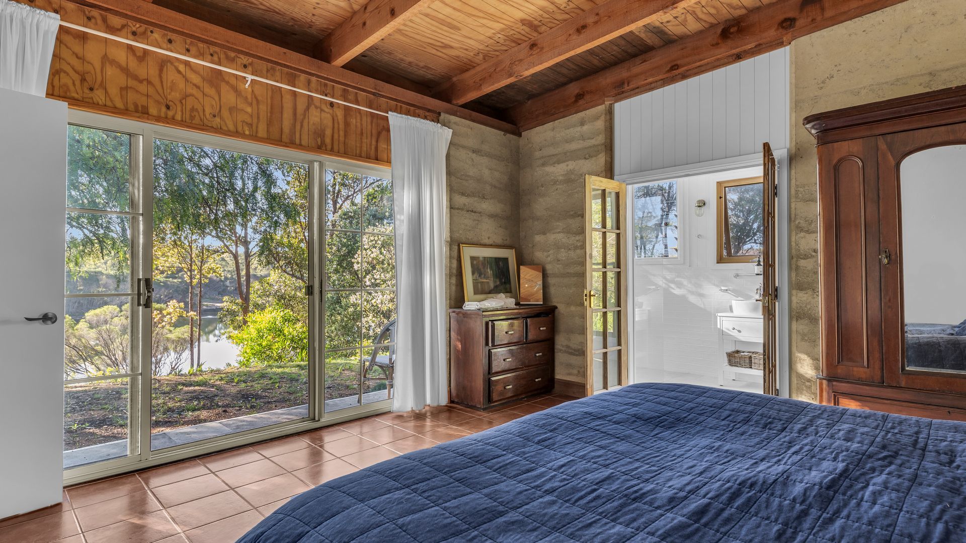 A bedroom with a large bed, a wooden dresser, and a sliding glass door leading to a garden.