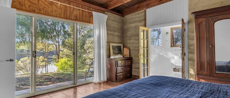 A bedroom with a large bed, a wooden dresser, and a sliding glass door leading to a garden.