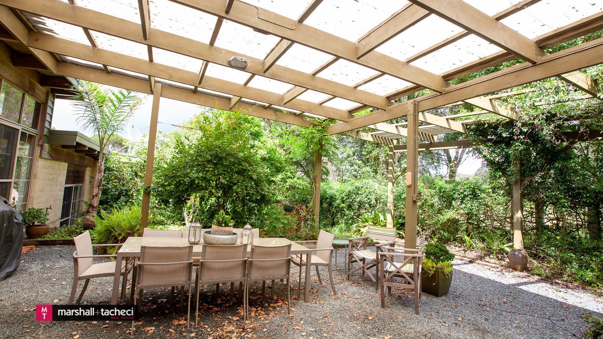 An outdoor patio with a pergola, tables, chairs, and potted plants.
