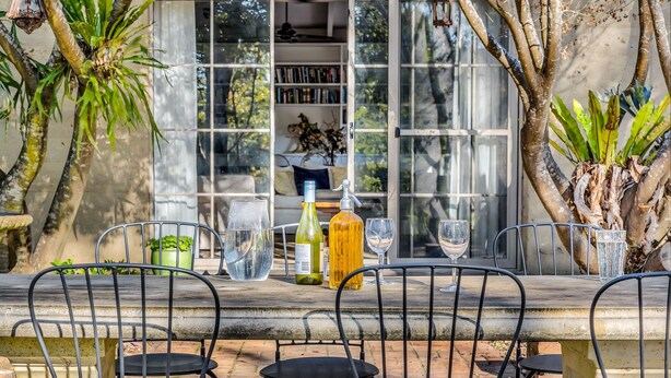 Un espace de restauration en plein air avec une longue table, des chaises et une variété de verres et de bouteilles.