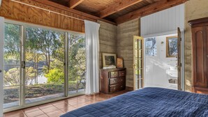 Une chambre avec une grande porte-fenêtre coulissante donnant sur un jardin, une commode en bois et une armoire.