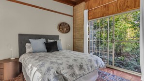 A bedroom with a large bed, a round wall shelf, and a view of greenery through a large window.