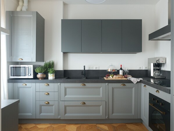 A modern kitchen with grey cabinets, a microwave, a coffee machine, and a wine bottle.
