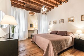 A bedroom with a wooden ceiling, a large bed with a pink quilt, a desk with a lamp, and a chair. - Venice apartment with breath-taking Grand Canal view (Venecia)