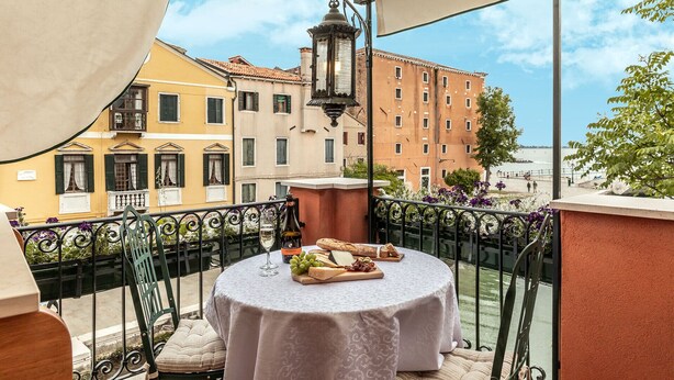 Un balcón con una mesa redonda dispuesta para una comida, con vistas a un paisaje urbano lleno de edificios históricos.