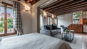 Un dormitorio con una cama grande, un sofá y una mesita. Hay ventanas con cortinas, vista al exterior y techo de madera.