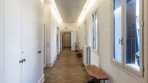 Un pasillo largo y estrecho con paredes blancas, piso de madera y amplias ventanas a un lado.