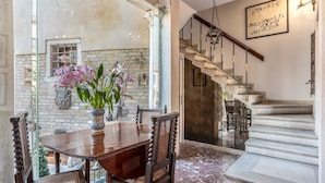 Uma sala de jantar com mesa e cadeiras de madeira, um vaso com flores e uma escada com lustre.