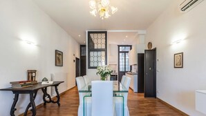 A dining area with a glass-top table, white chairs, and a chandelier. - San Marco Alluring and Spacious Apartment with Elevator (Venecia)