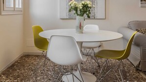 Un comedor con una mesa redonda, dos sillas, un florero con flores y una lámpara colgante.
