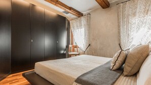 Quarto com cama, um banco de madeira, uma cadeira e um guarda-roupa.