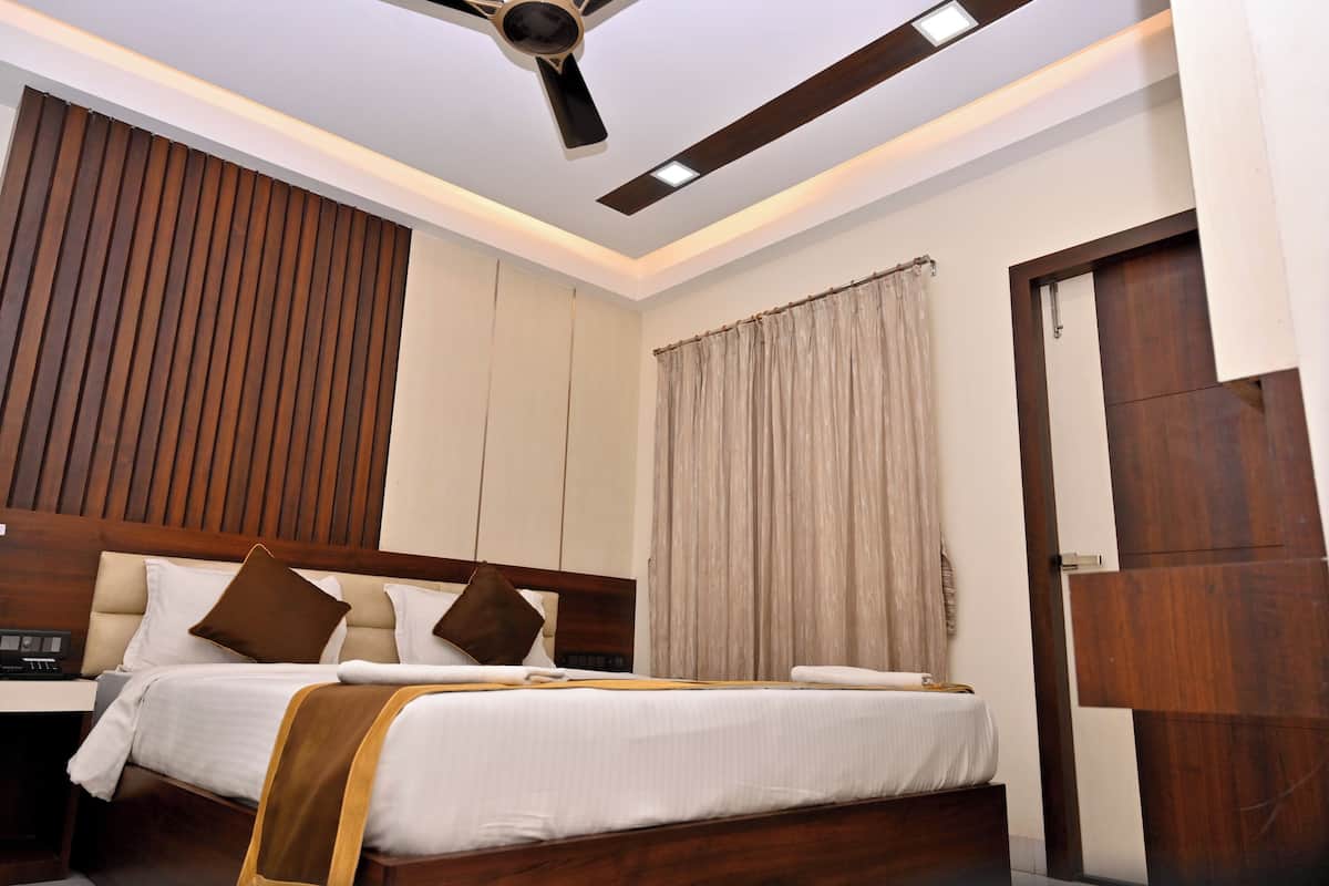 Una habitación de hotel con dos camas, un ventilador de techo, un cabecero de madera, una mesita de noche y un amplio ventanal con cortinas.