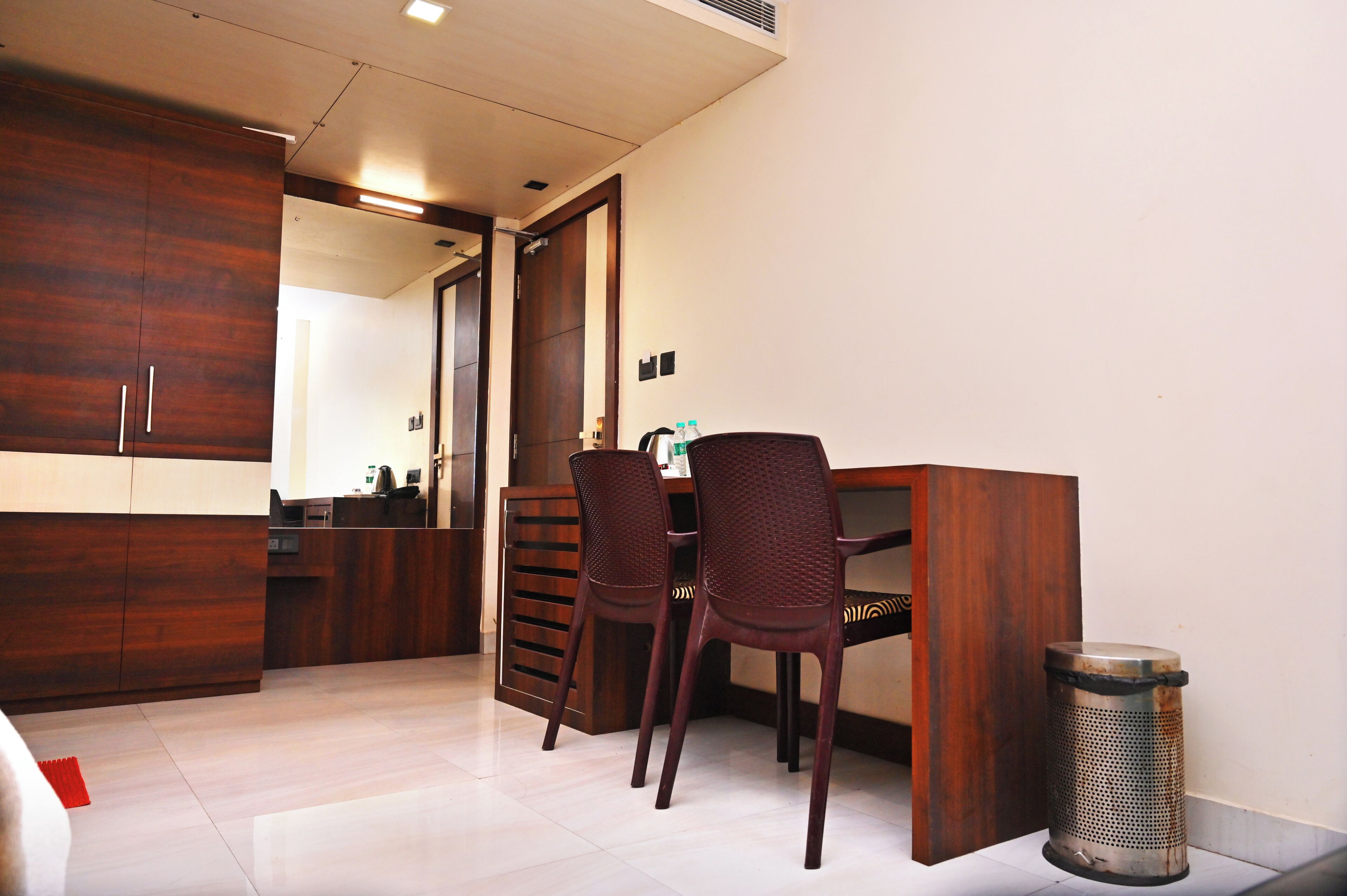 Habitación de hotel con escritorio de madera, dos sillas, un cesto de basura y un espejo.