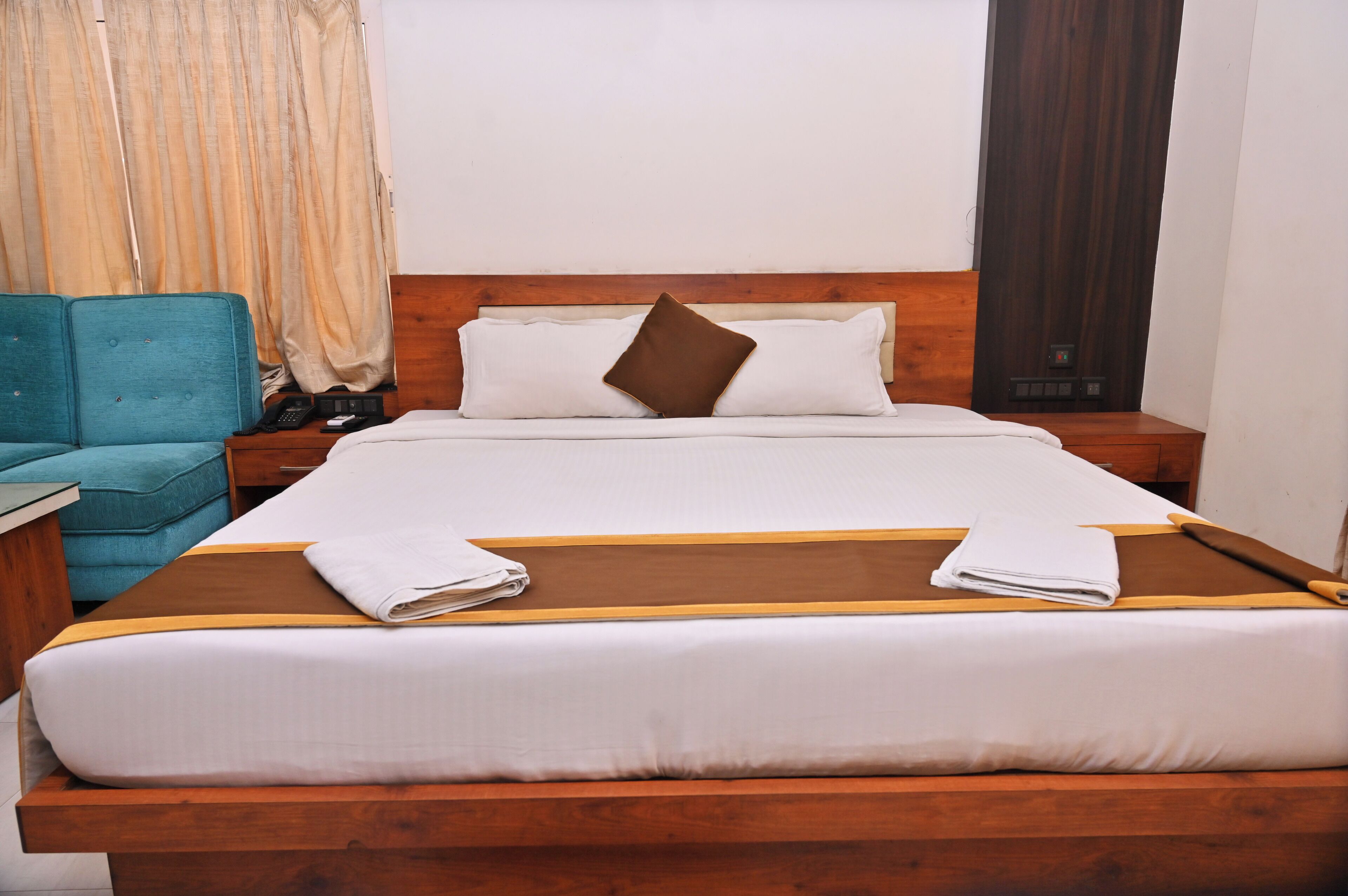 A neatly made bed with white linens and a brown pillow, a wooden headboard, a blue armchair, and a nightstand with a phone and a lamp.