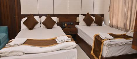 A hotel room with two beds, each with a wooden headboard, white bedding, and brown pillows. There is a wooden nightstand with a phone and a remote control, and a teal chair.
