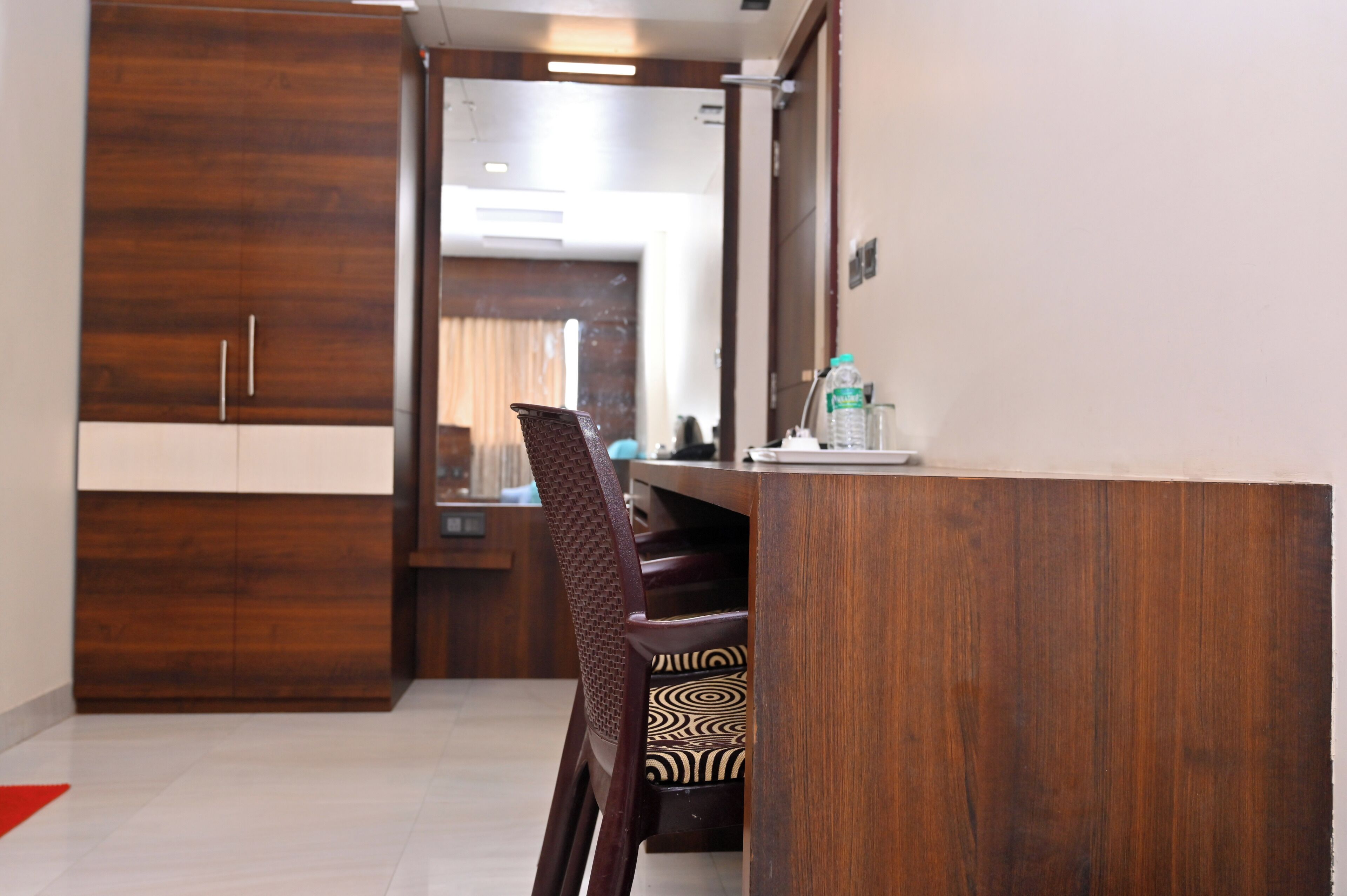 A modern hotel room with a wooden wardrobe, a desk with a chair, and a mirror.