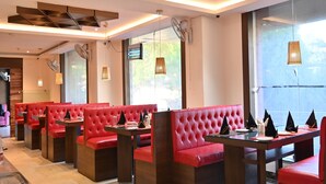 A modern restaurant with red upholstered booths, pendant lighting, and a geometric ceiling design.