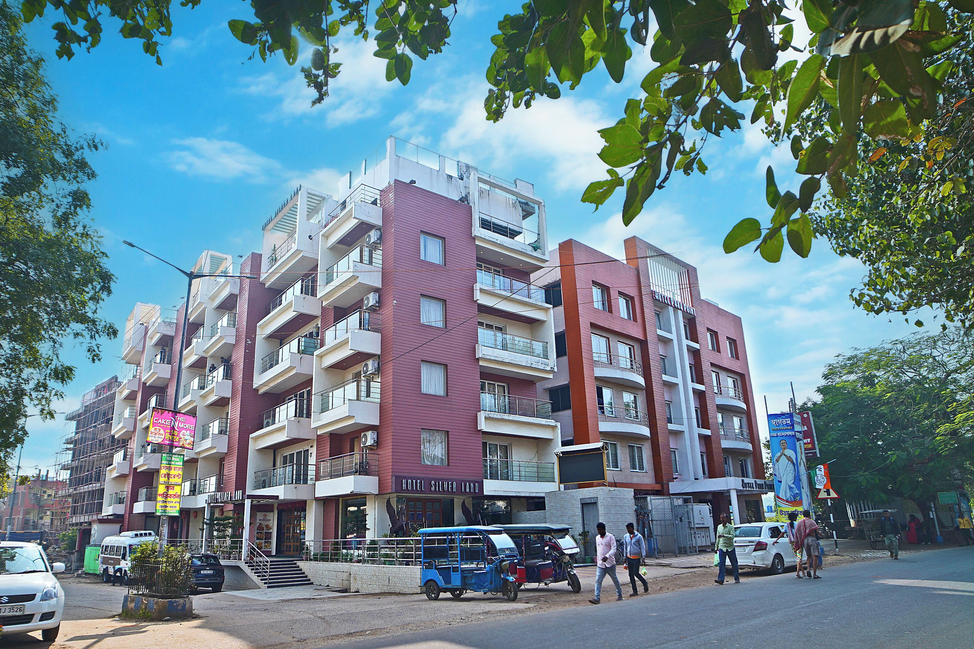A multi-story hotel with balconies, a sign for 'Hotel Silver Land', and a street with pedestrians and vehicles.