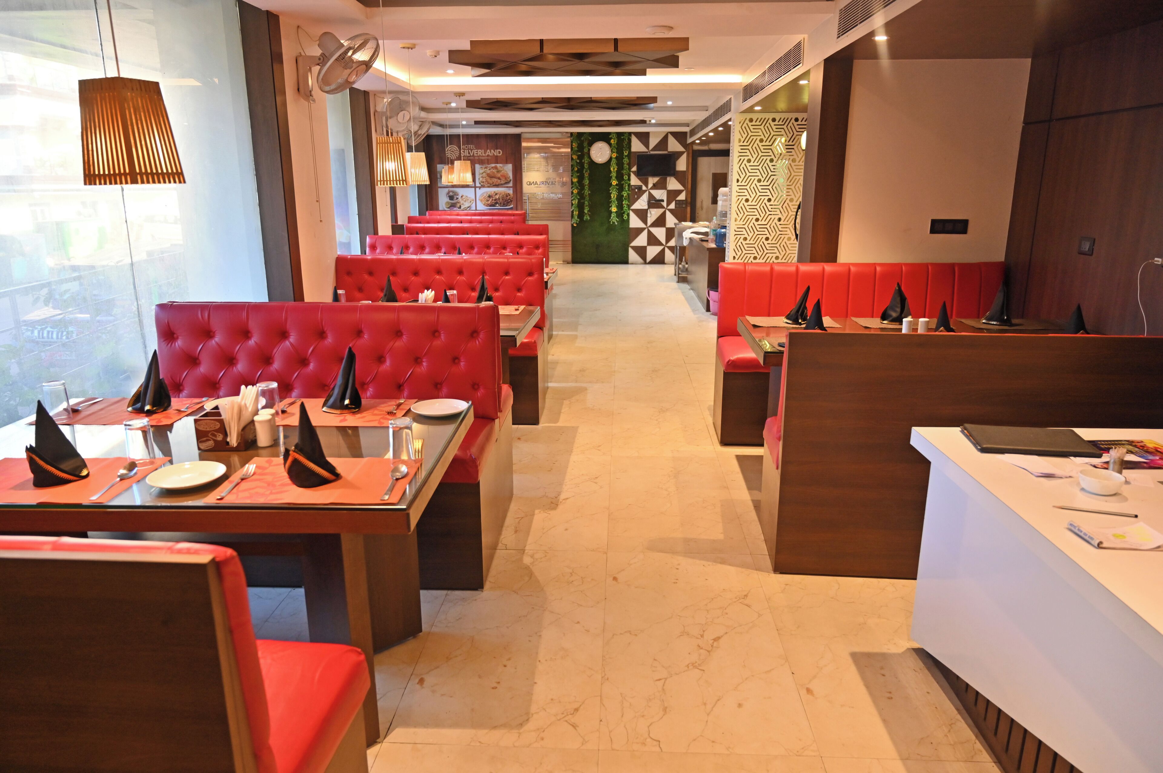 Interior de un restaurante con cabinas tapizadas de rojo, un mostrador de recepción y vista a la calle.
