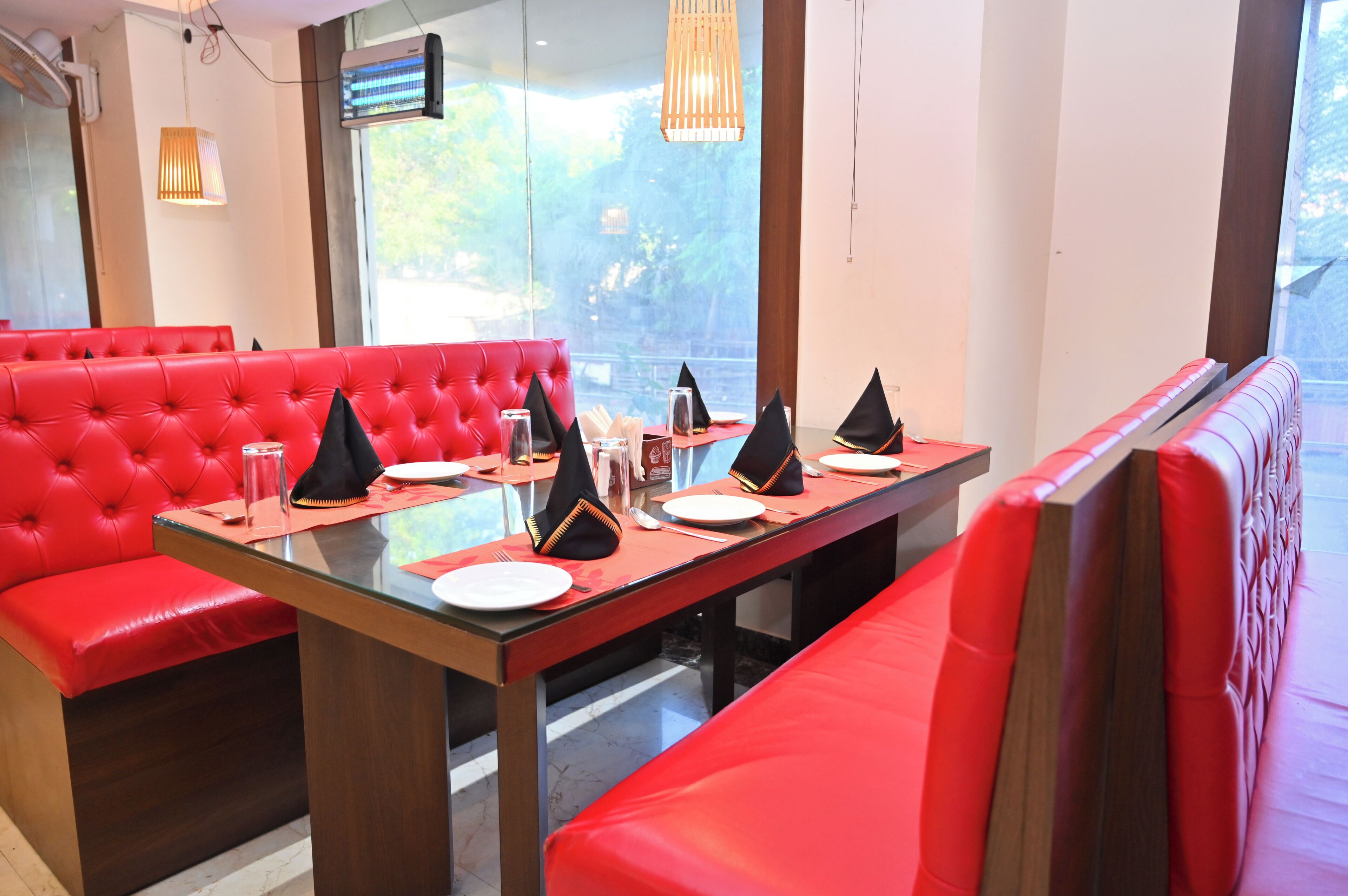 Uma área de refeições com assentos estofados em vermelho e uma mesa comprida posta para dois.