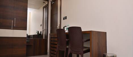 Una habitación de hotel con un armario de madera, un escritorio con dos sillas, un cubo de basura y un espejo.