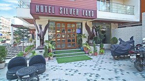 A hotel entrance with a sign reading "HOTEL SILVER LAND," a covered motorcycle, potted plants, and outdoor seating.
