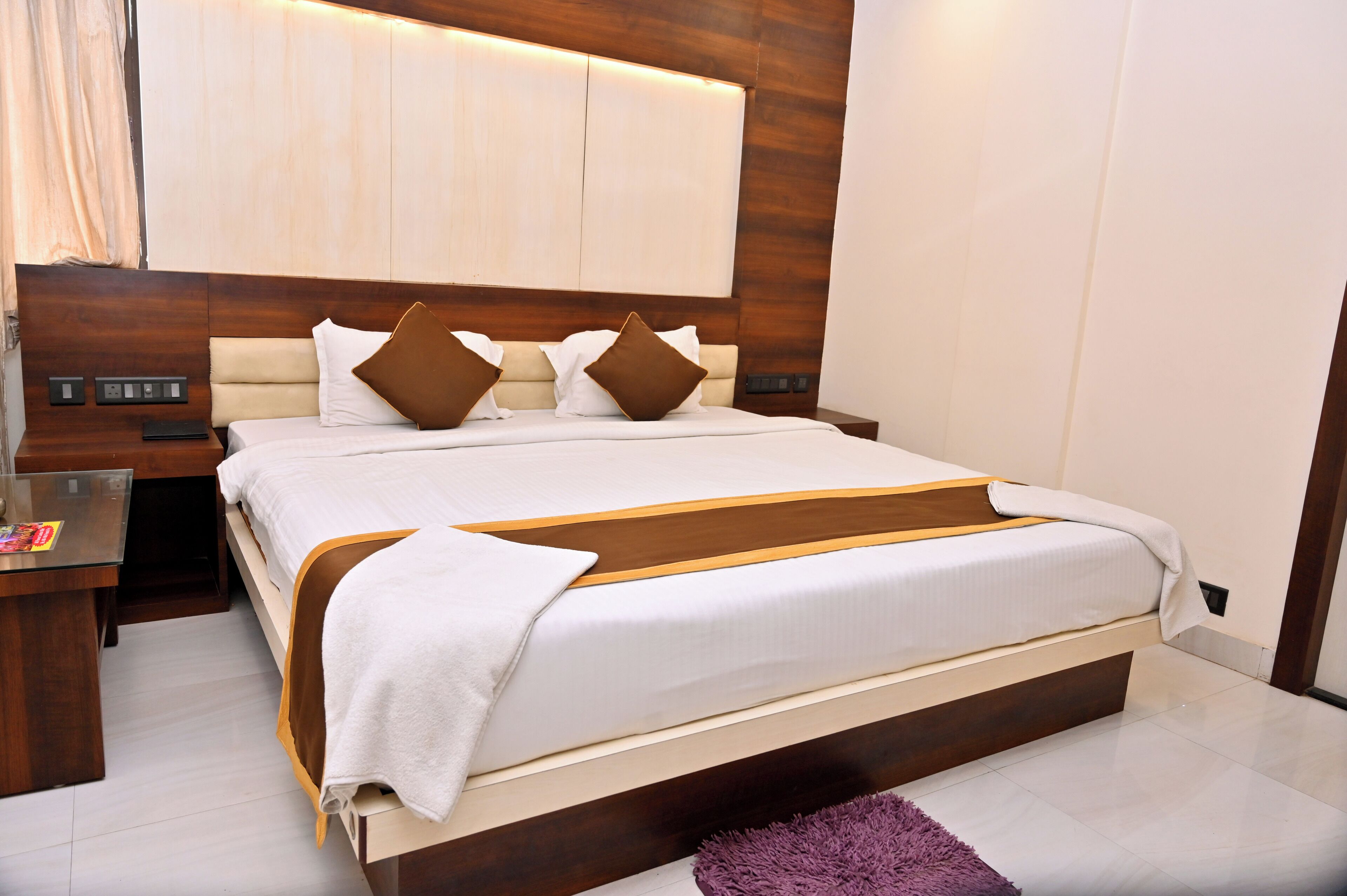 Una habitación de hotel moderna con una cama grande, cabecera de madera y una mesita de noche con lámpara.