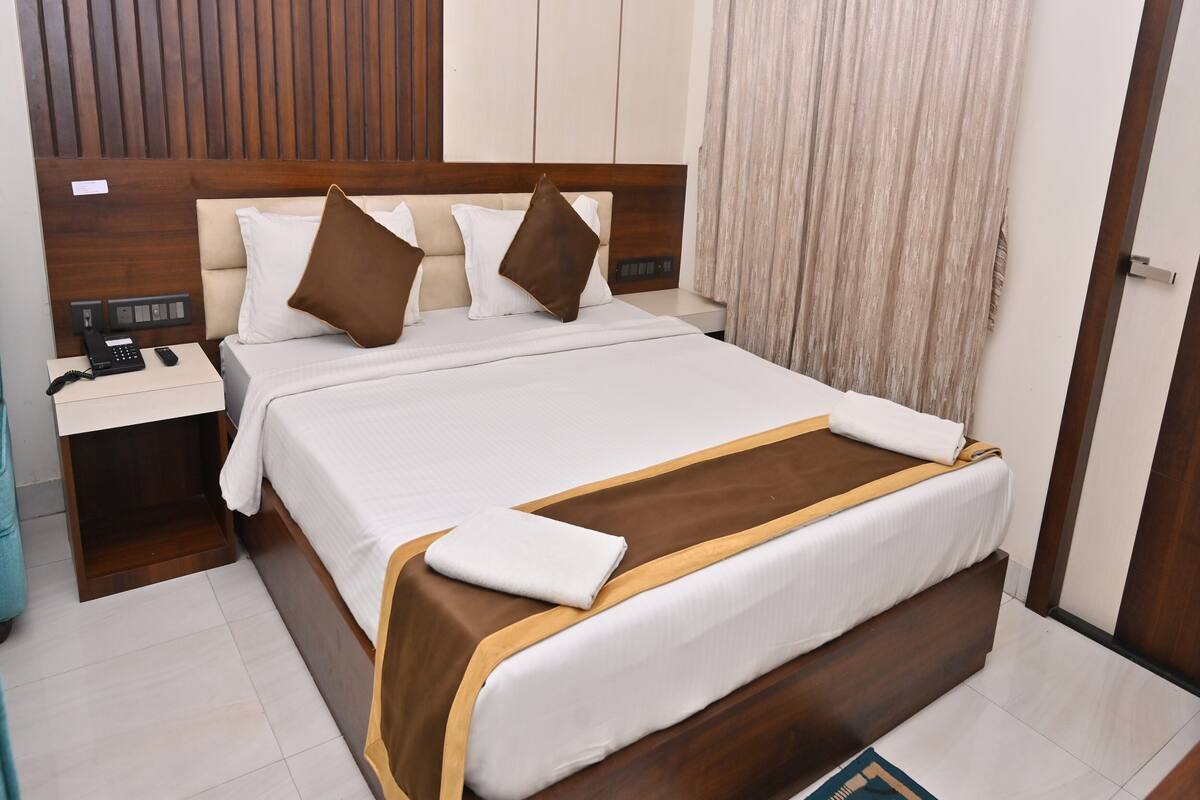 Una cama bien hecha con un cabecero de madera, una mesita de noche con un teléfono, y una alfombra pequeña en el suelo.