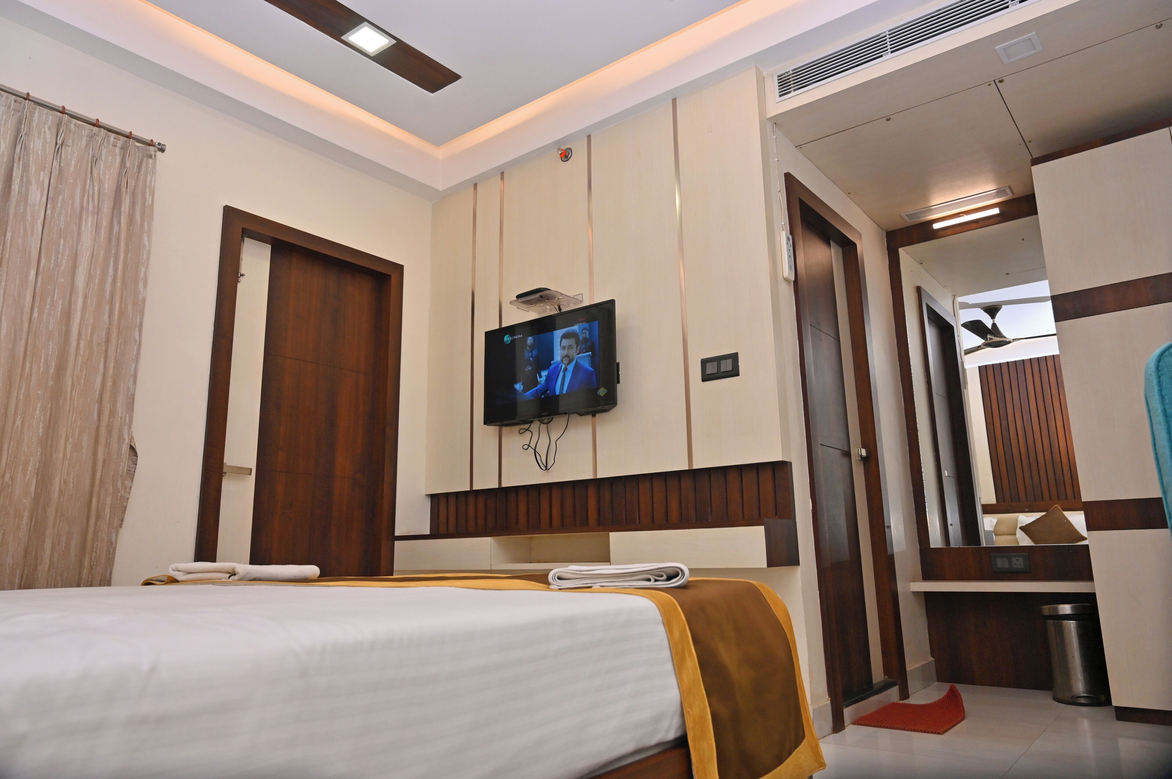 A hotel room with a bed, a TV mounted on the wall, a wooden door, and a small table with a towel.