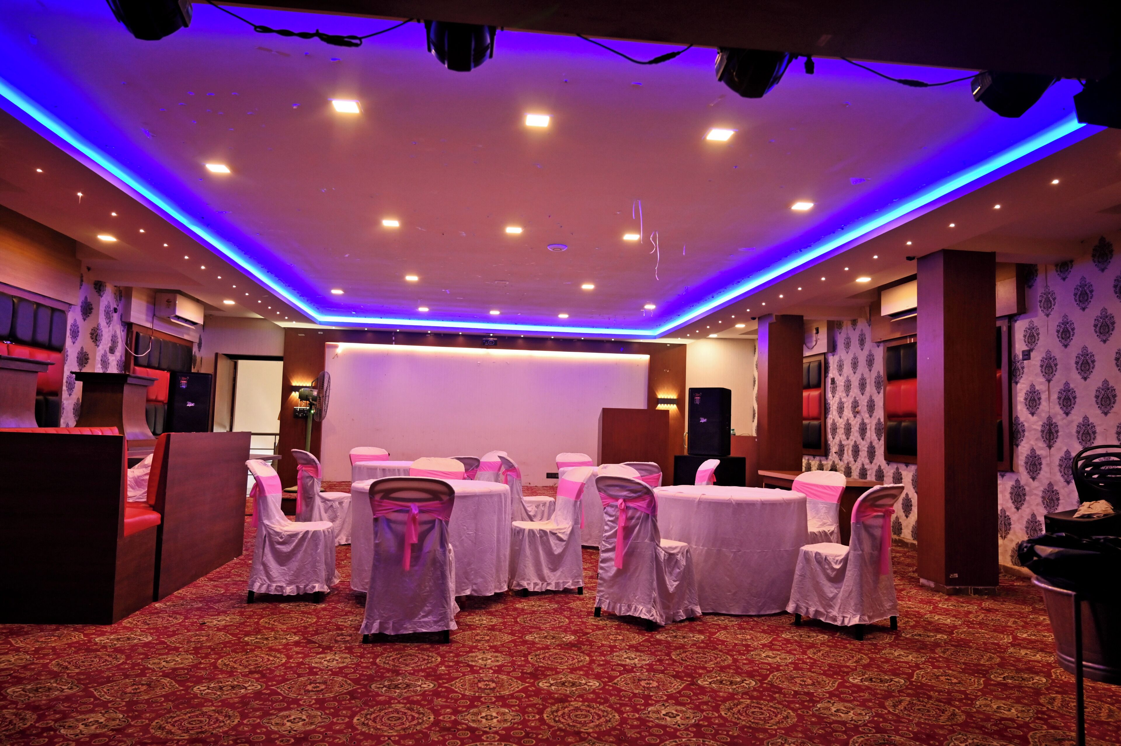 A banquet hall with round tables and chairs, a stage, and patterned wallpaper.