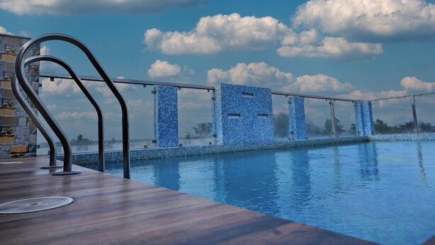 A pool area with a wooden deck and a view of the sky and clouds.