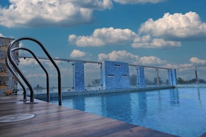 Zona de piscina con terraza de madera y vista al cielo y nubes.