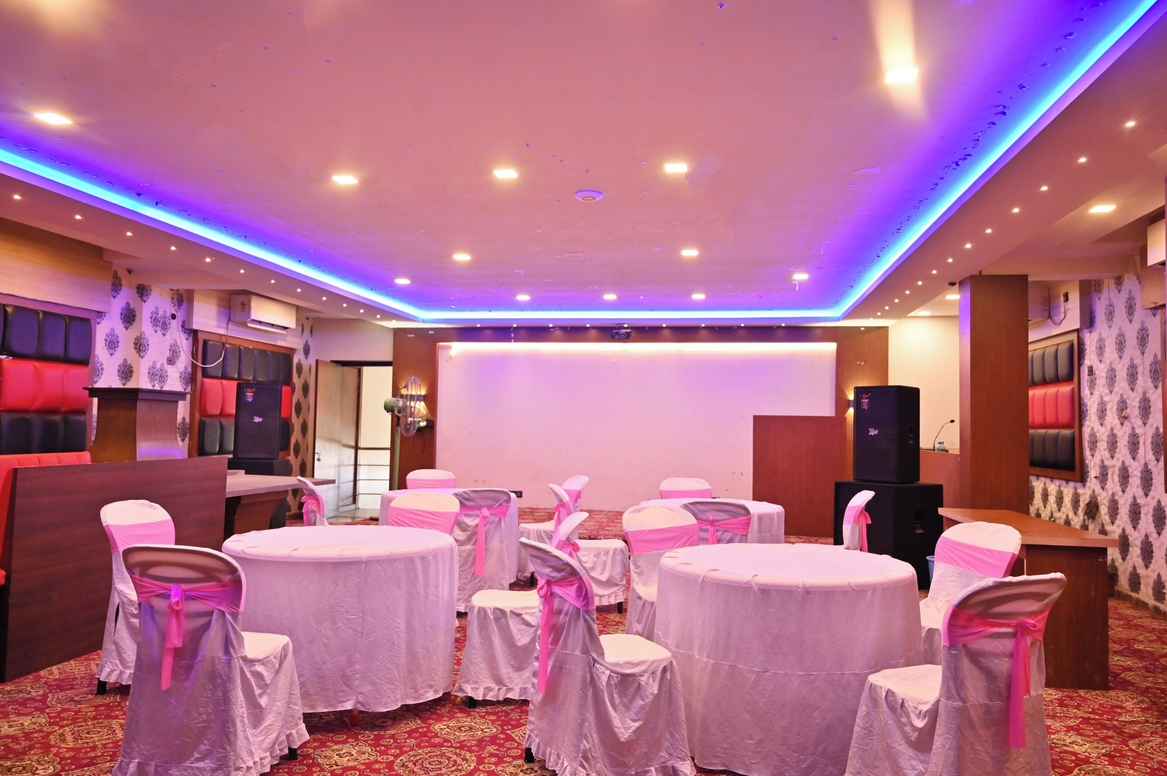 A conference room with round tables, chairs with pink sashes, and a stage with a white backdrop.