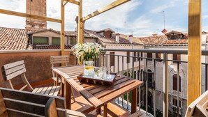 A wooden balcony with a table and chairs, overlooking a cityscape with terracotta roofs and a historic tower. - Distinctive Penthouse with Elevator Terrace and View (Venecia)