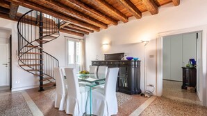 A dining area with a glass table and chairs, a spiral staircase, and a kitchen area with cabinets and a countertop. - Distinctive Penthouse with Elevator Terrace and View (Venecia)