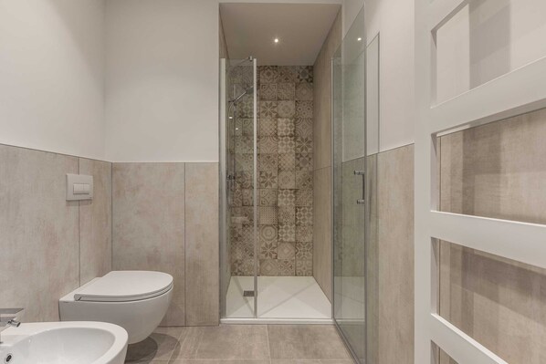 A modern bathroom with a toilet, a bidet, and a glass-enclosed shower area.