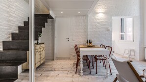 Un coin repas avec une table dressée pour quatre personnes, un escalier en bois et un mur en briques blanches.
