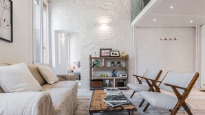 Un salon chaleureux avec un mur en briques blanches, une table basse en bois, un canapé et une bibliothèque agrémentée d’objets décoratifs.