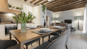 Een moderne keuken met houten balken, een eethoek met een lange tafel, en een woonruimte met televisie en bank.