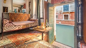 A cozy room with a patterned sofa, a small wooden table with snacks and wine glasses, and a view of a courtyard with a pool. - Unconventional Loft Style Apartment in San Barnaba (Venecia)