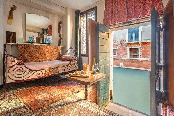 A cozy room with a patterned sofa, a small wooden table with snacks and wine glasses, and a view of a courtyard with a pool. - Unconventional loft-style apartment in San Barnaba (Venecia)