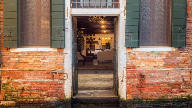 A brick building with a waterway in front, a door with green shutters, and a staircase leading inside. - Unconventional Loft Style Apartment in San Barnaba (Venecia)